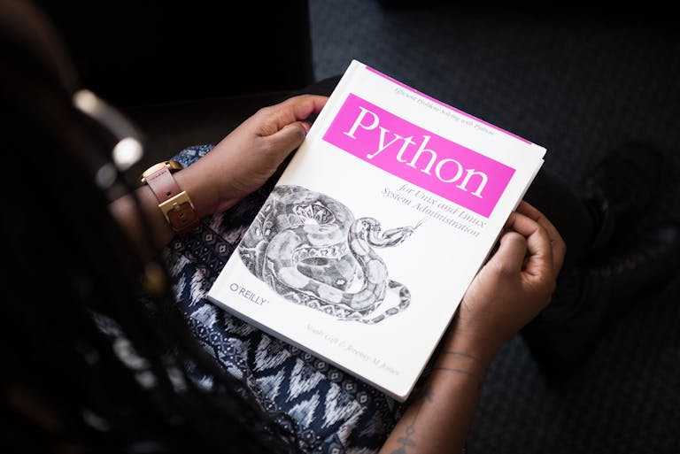 A person reads 'Python for Unix and Linux System Administration' indoors.