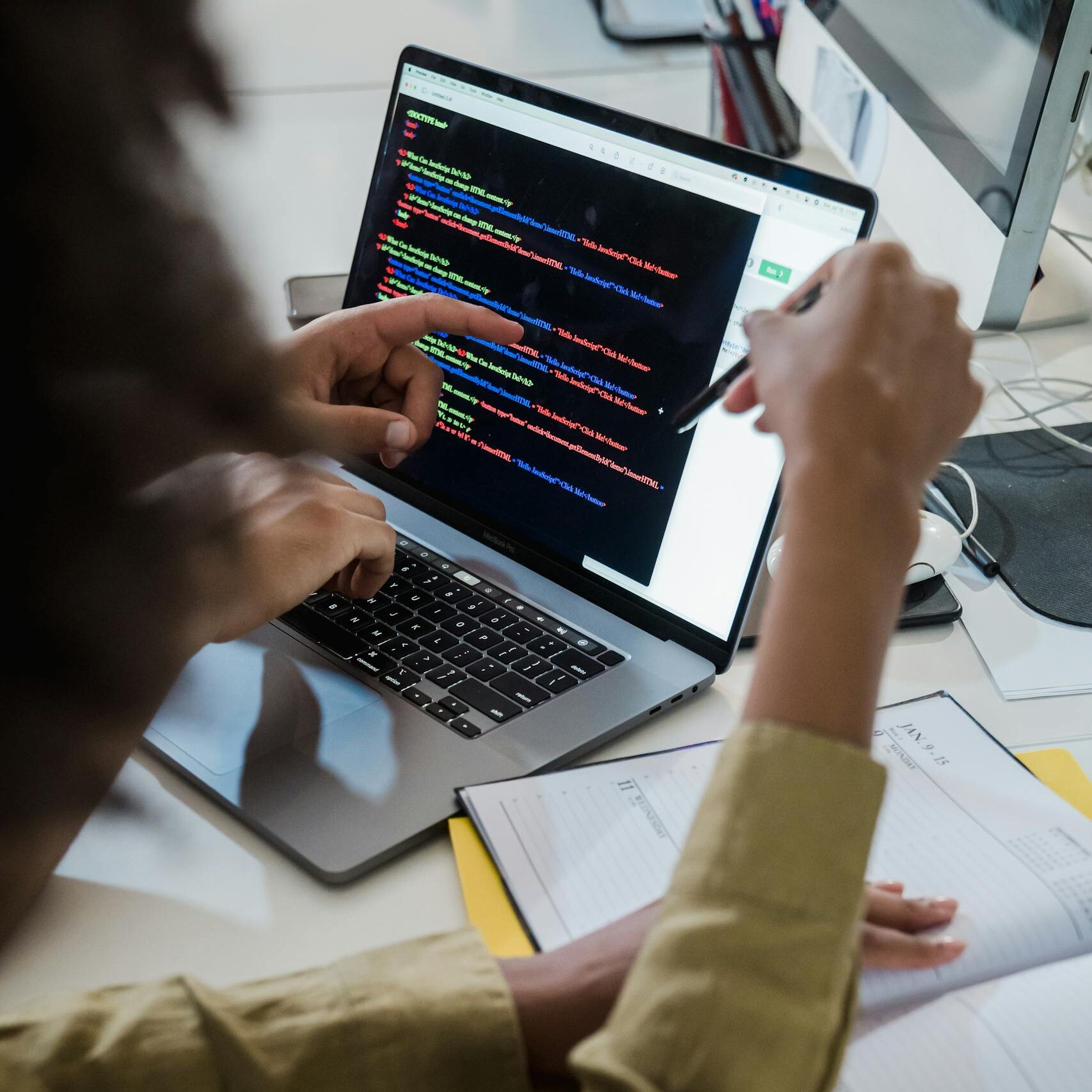 Two individuals discussing code on a laptop, focusing on web development.